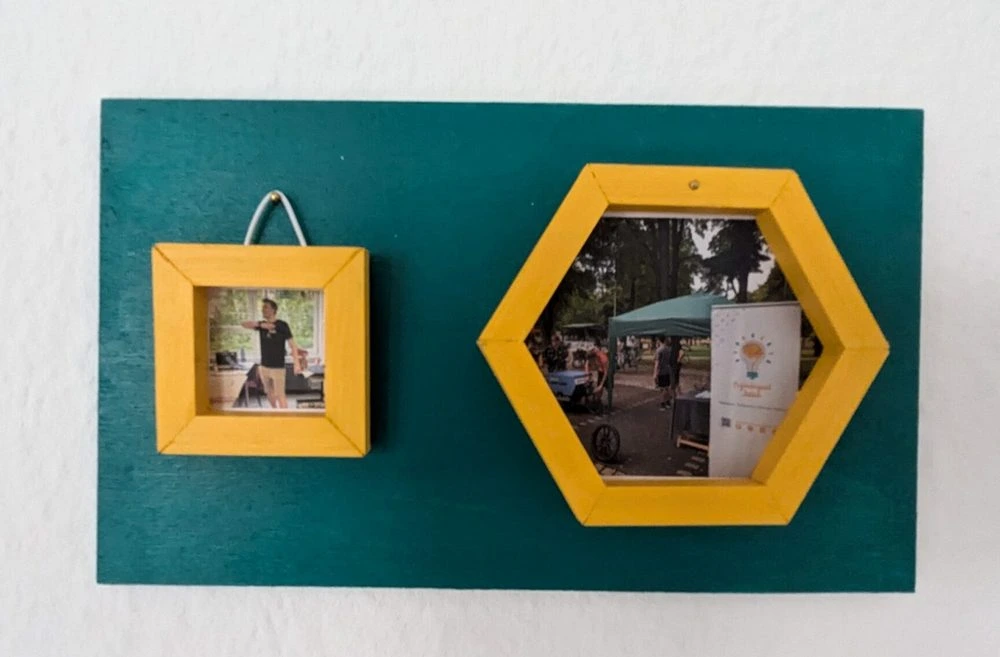 In den Bilderrahmen sind Fotos vom Verein. im viereckigen ist ein Bild vom Roboworkshop, welches Johannes zeigt. Im sechseckigen ist ein Bild vom Mobilitätstag welches unseren Stand dort zeigt. Und das ganze hängt nun an einer Wand.