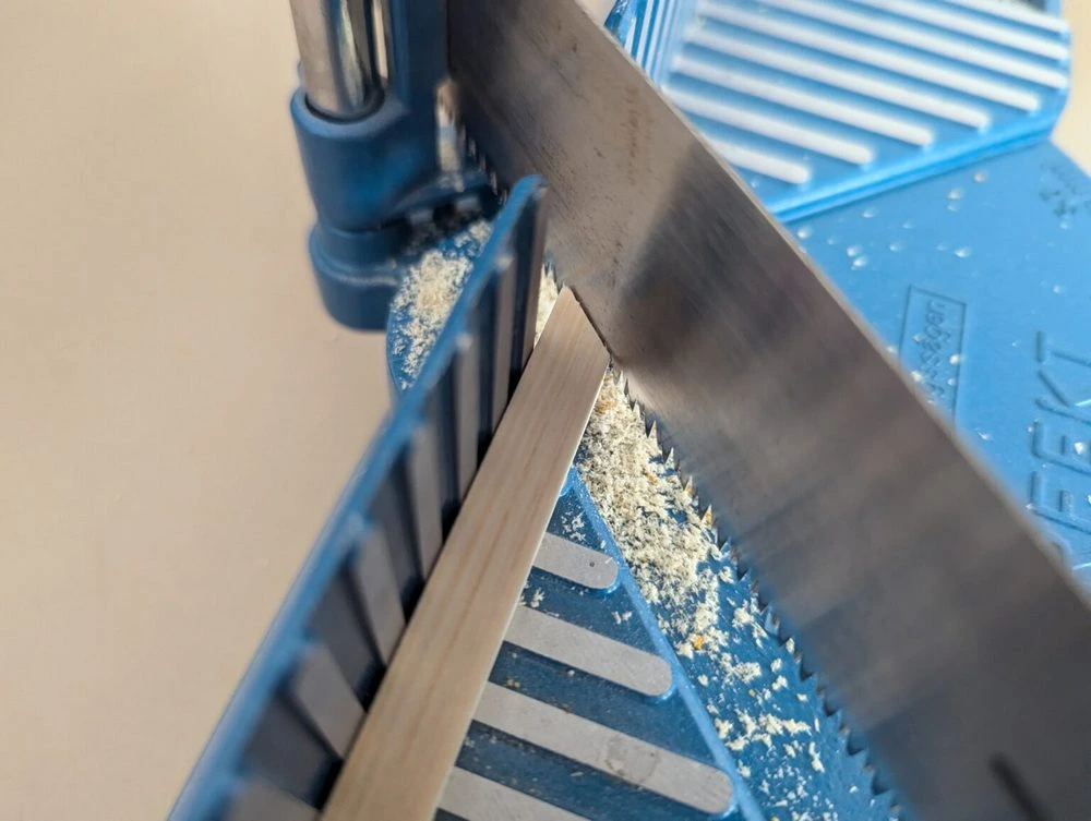 Ein rechteckiges Stück Holz liegt in einer Gehrungssäge und wird in einem 45° Winkel zersägt